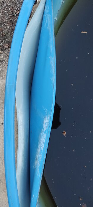 Deformerad blå poolkant med synliga veck och smutsigt vatten. Skador från tidigare översvämning.