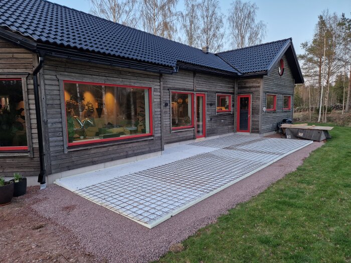 Byggprojekt med isolering och nät på marken framför ett hus i trä.