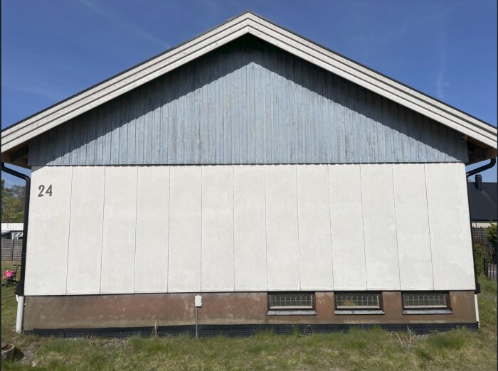 Eternitfasad med nummer 24, delvis ljusblå träpanel på övre delen och vita paneler nedtill.