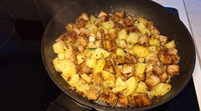 Stekt pyttipanna med potatis och köttbitar i en stekpanna.