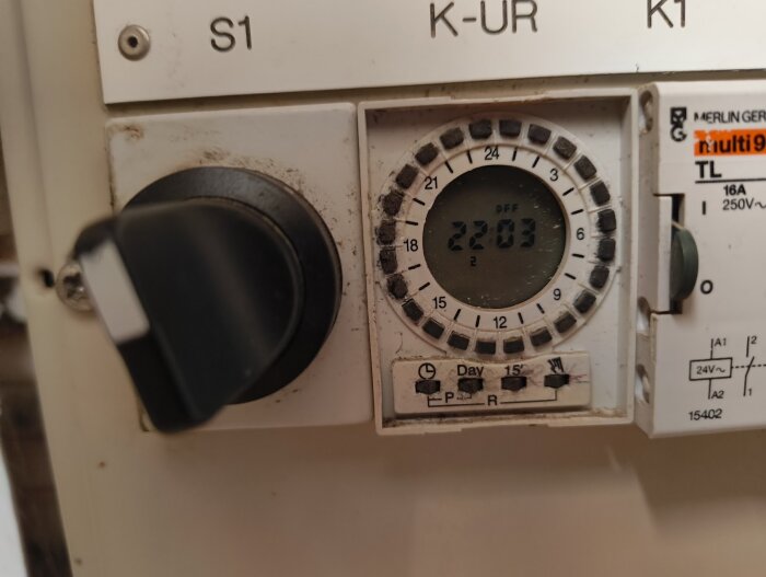Timer installerad i en elcentral, inställd på 22:03, med vred och inställningsknappar för tid och dagar.