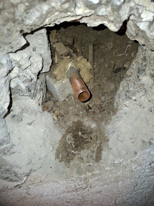 Ett exponerat kopparrör i ett hål i en vägg, omgett av isolering och skrovlig murverk.