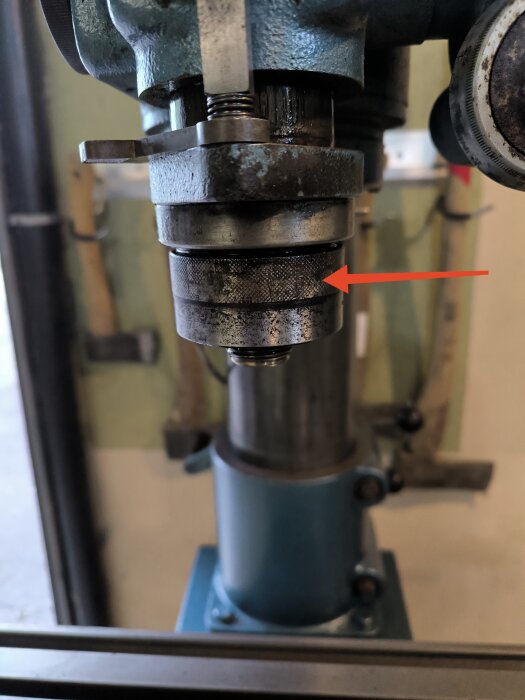 Bilden visar en borrmaskin med en fokus på en mutter som behöver lossas, markerad med en röd pil.