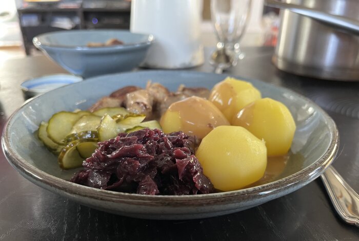 Tallrik med köttbullar, kokt potatis, brunsås, rödkål och inlagd gurka.