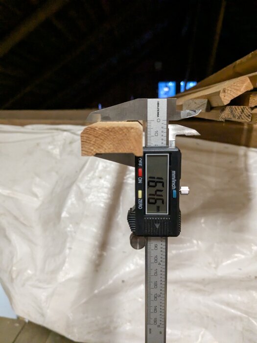 En digital skjutmått mäter en träbit till 15,46 mm i tjocklek.