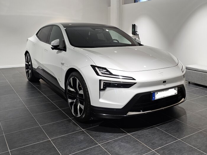 Vit bil i ett showroom med svarta plattor, parkerad snett framifrån, med pärlemoeffekt och futuristisk design.
