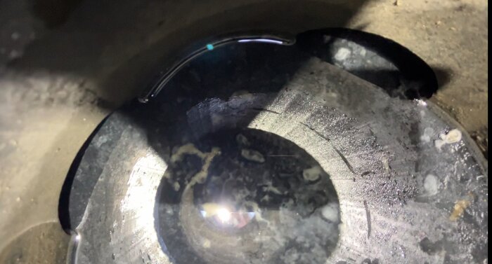 Uppsamlingsbrunn med klart vatten ovanpå svart lera och vitt slam på botten, belyst med ficklampa.