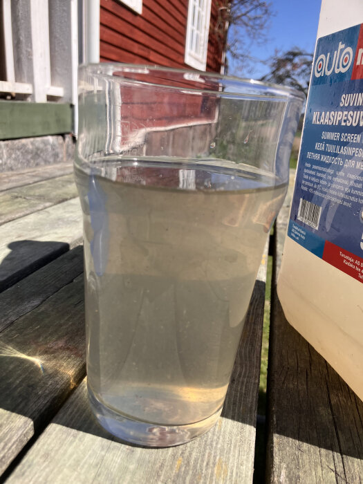 En glasbehållare med grumligt vatten från ett utlopp, placerad på ett träbord bredvid en plastflaska.