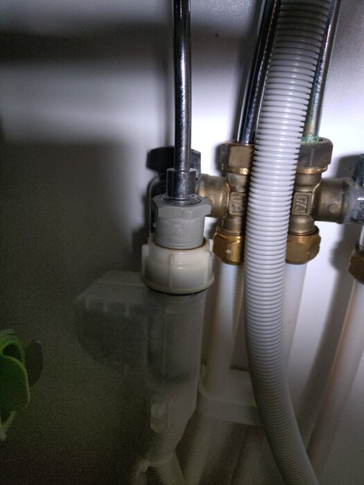 Vattenanslutningar under diskbänk med metallrör, ventiler och plastslangar i ett kök.