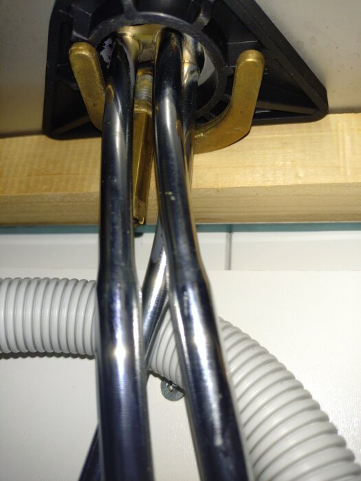 Diskmaskinens vattenanslutning under diskbänken med metallrör och en plastslang, nära en avstängningsventil.