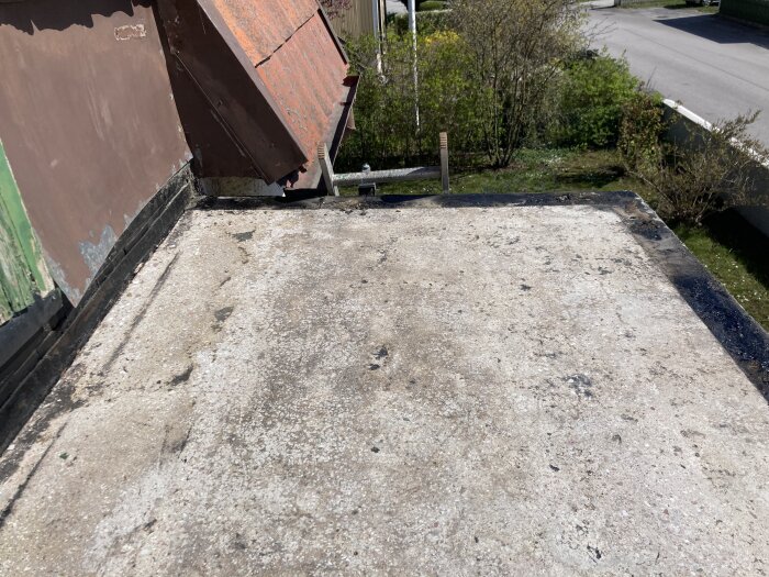 Balkong med slipad, ljus betongyta och borttagen gummiduk, belägen ovanför veranda med vy över grönska och gata.