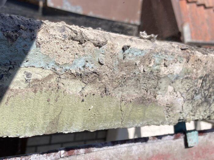 Närbild av en gammal balkongkant i gjuten betong med färgrester och ytskador, taken syns i bakgrunden.