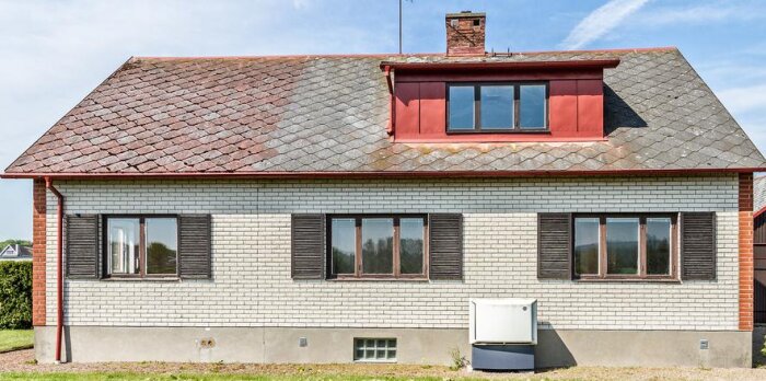 Fasad av ett enfamiljshus i tegel med sadeltak, tvåglasfönster och enkel entrédörr, 1,5 plan med källare.