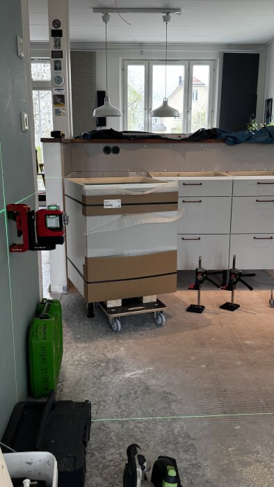Kök med bänkskåp på hjulplattform, grön laserlinje, två hängande lampor och byggutrustning.