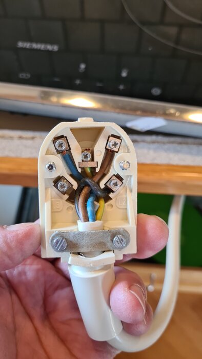 Elkontakt med fem anslutningar där kablarna är fastskruvade; en grå kabel är klippt och inte ansluten. Bakgrund visar etiketten "Siemens".