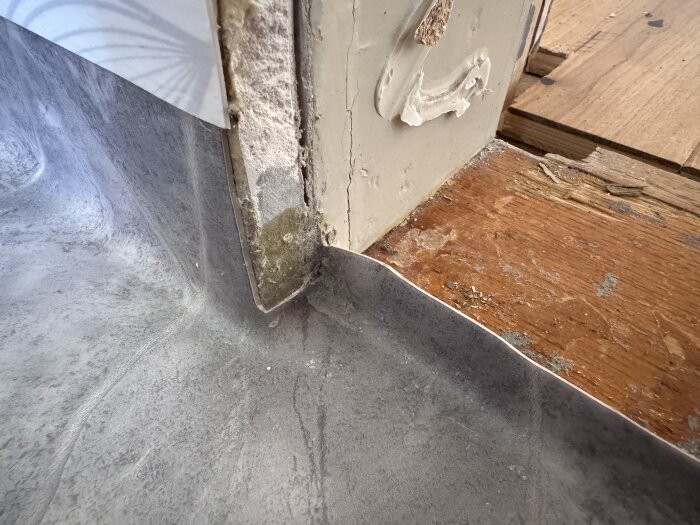 Våtrumsmatta vid dörrkarm med snitt och uppvikt kant samt synliga skarvar, intill trätröskel, med silikon över skurna kanter.