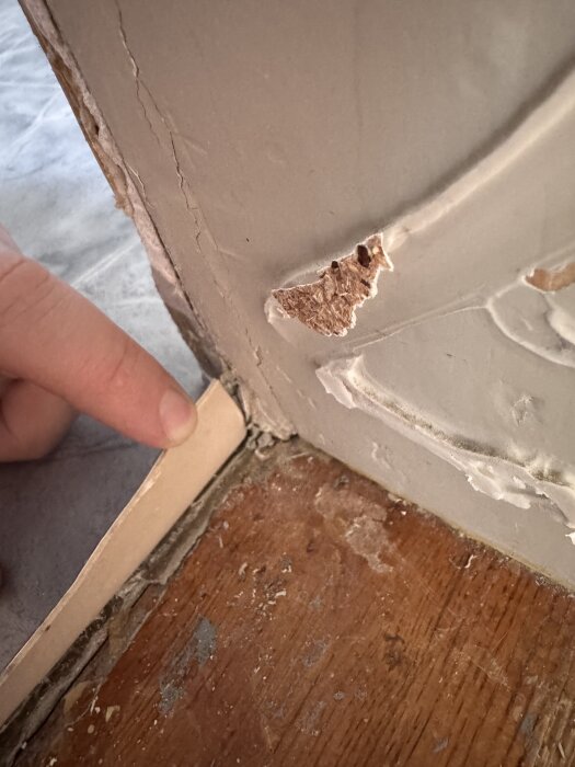 Hand pekar på avlägsnad tröskel, exponerar våtrumsmatta och snitt i hörnen, med silikonfogar längs kanten vid badrumsdörr.