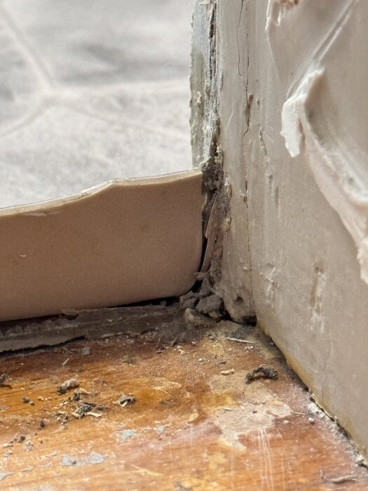 Våtrumsmatta vid tröskel, skuren i hörnet, silikon över snitt, matta viks uppåt. Trä och vägg syns, bilden visar snittets utförande och eventuella skador.