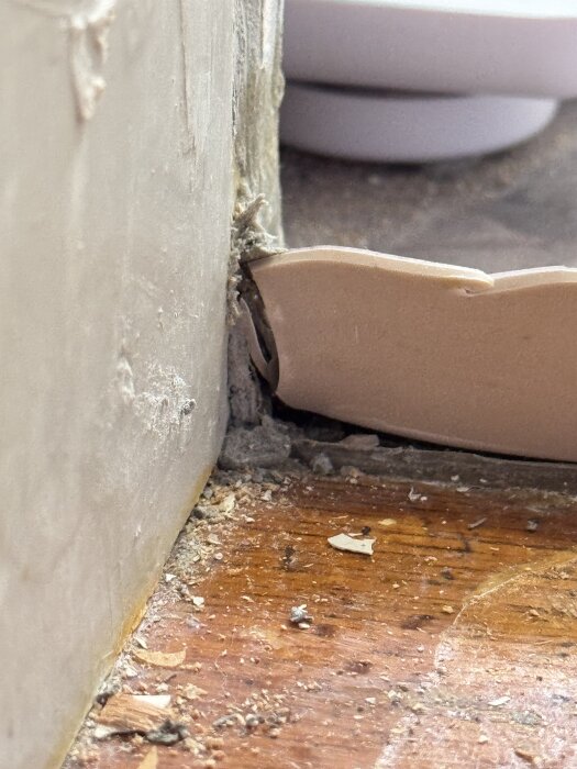 Våtrumsmatta skuren i hörn vid tröskel med synlig silikon och byggdamm, påträffad i ett badrum under renovering.