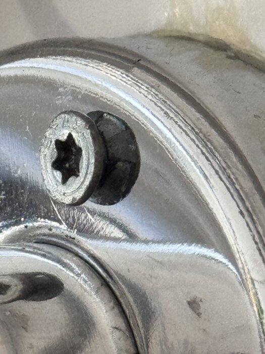 Handdukstork monterad med en stjärnskruv i kromat metallfäste, visas på nära håll för att illustrera mix av skruvtyper i konstruktionen.