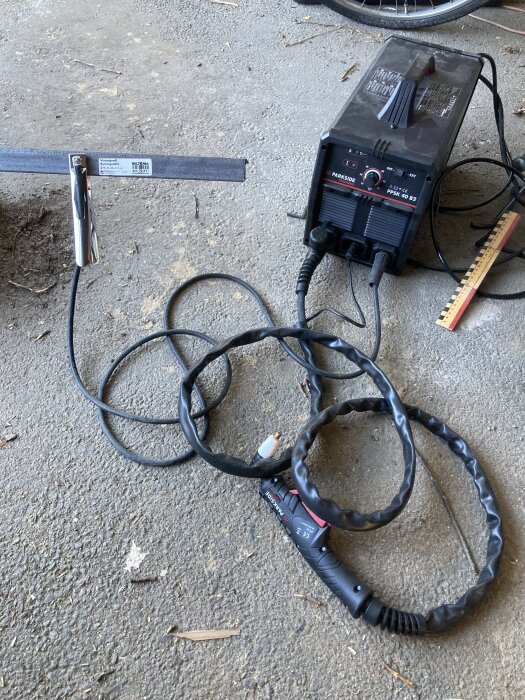 Plasmaskärare och vinkeljärn på betonggolv, redo för kapning. Verktyg, sladdar och mätverktyg synliga.