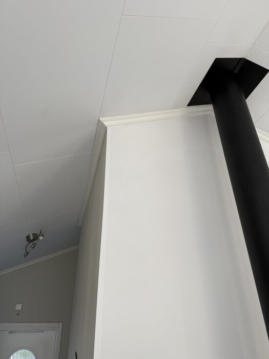 Hjørne av rom med nyinstallerte lister rundt en skorsteinpipe. Vegglistene er nøyaktig tilpasset og malt i hvitt, med en moderne innredning.