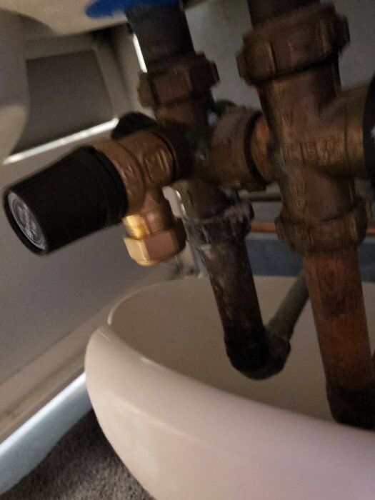 Vattenventil med läckage vid skruvanslutning under varmvattenberedare, omgiven av olika rör och komponenter.