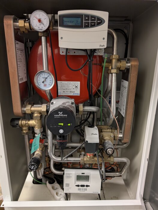 Fjärrvärmecentral med olika ventiler och mätare, inklusive en Danfoss reglerventil och elektronisk display.