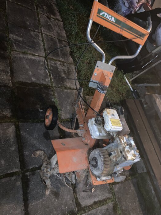 En äldre orange Stiga jordfräs med Briggs & Stratton motor, synlig på en stenlagd yta.