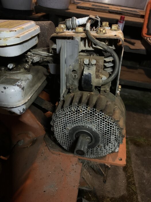 Bild på en Briggs & Stratton-motor till en jordfräs med synligt tändstift och svänghjul, delvis rostig och använd men hel.