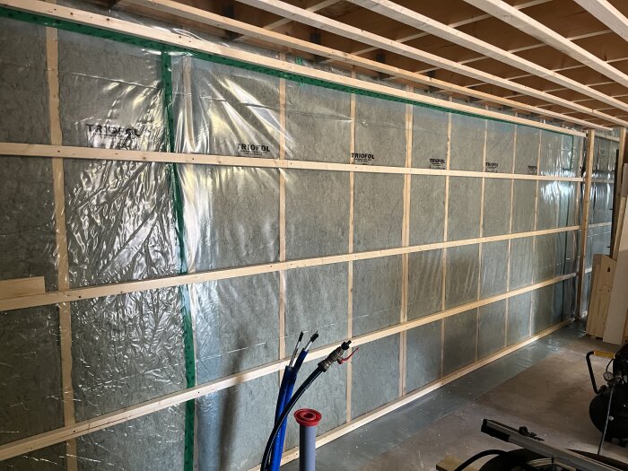 Vägg med isolering, stående reglar och plastfolie. Elektriska kablar och verktyg i förgrunden, del av pågående renoveringsprojekt.