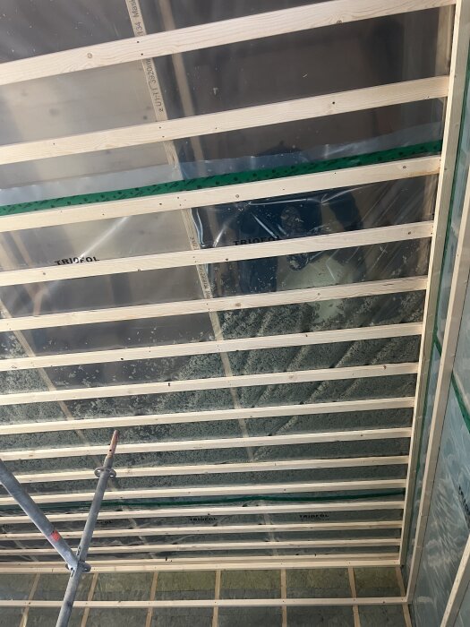 Väggar med isolering, plastskikt och träreglar samt tak med isolerande lösull syns. Pågående elarbeten.