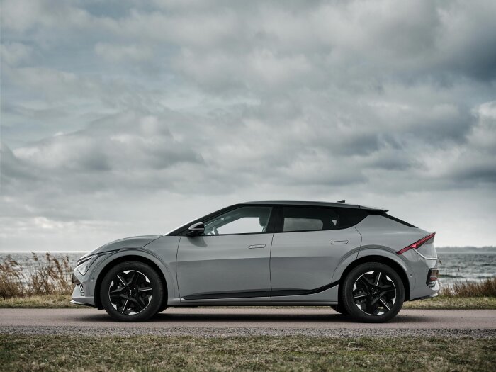 Silverfärgad Kia EV6 AWD 2025 står parkerad vid en kustväg under en molnig himmel, med havet i bakgrunden.