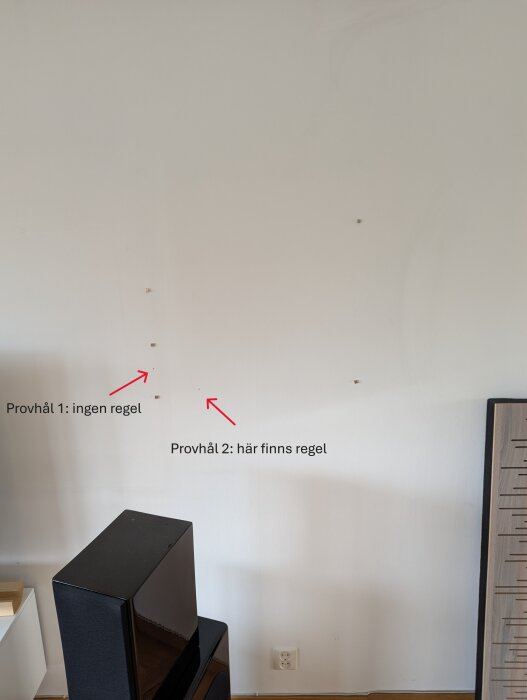 Vägg med två provhål, varav ett funnit en regel. Röda pilar markerar platsen för varje hål.