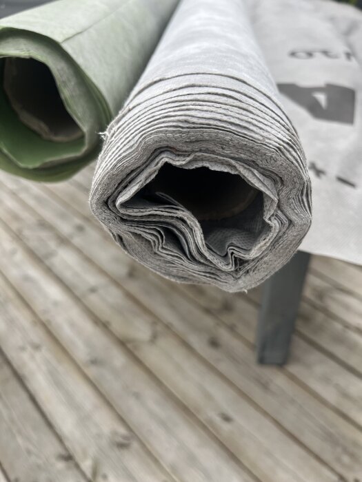 Två rullar byggmaterial, en grön och en grå, liggande på ett träbord.