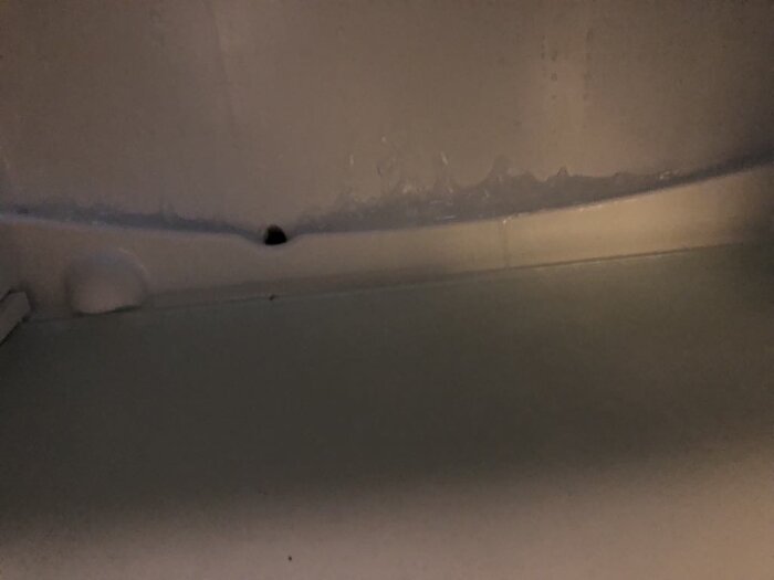 Isbildning i rännan bakom grönsakslådan i kylskåpet.