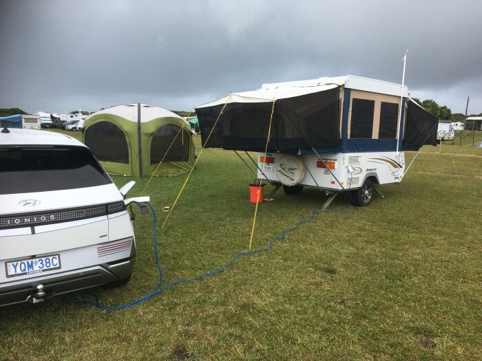 En bil laddar en husvagn på en campingplats; ett grönt tält och husvagnar syns i bakgrunden.