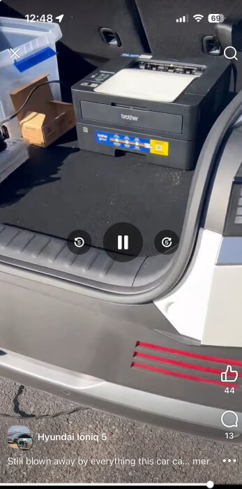 Brother-skrivare i bagageutrymmet på en Hyundai Ioniq 5 tillsammans med plastlåda och kartonger, fotograferat i solen.