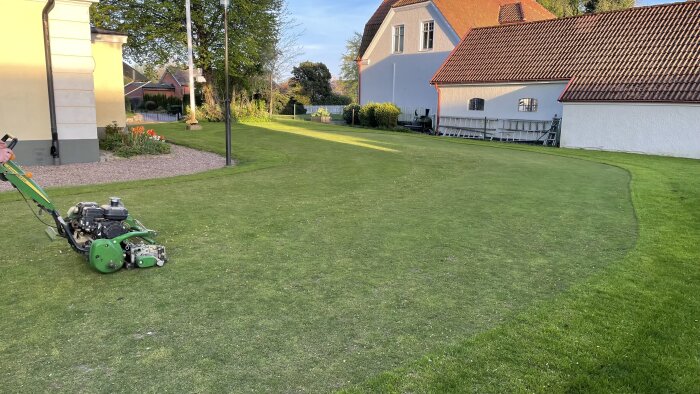 Gräsmatta efter klippning, med synlig gräsklippare, intill ett hus och trädgårdsland.