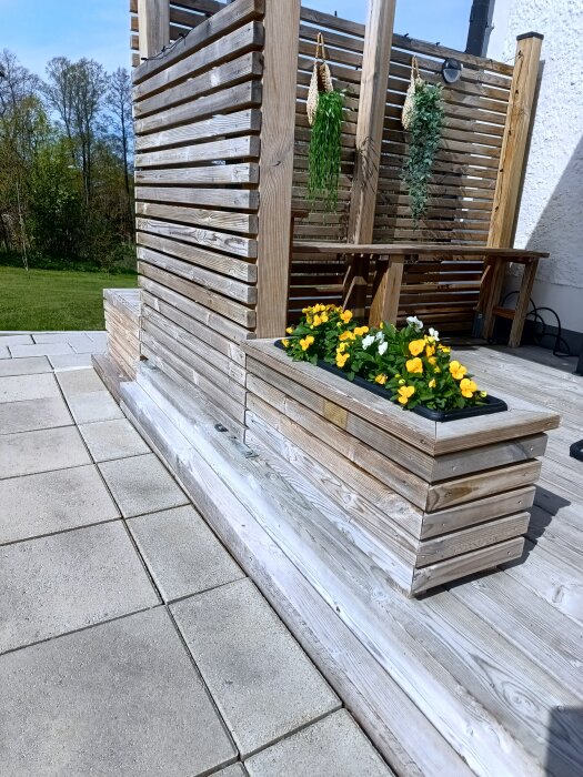 Blomlåda med gula och vita blommor på trätrall, med en trävägg i bakgrunden och hängande växter.