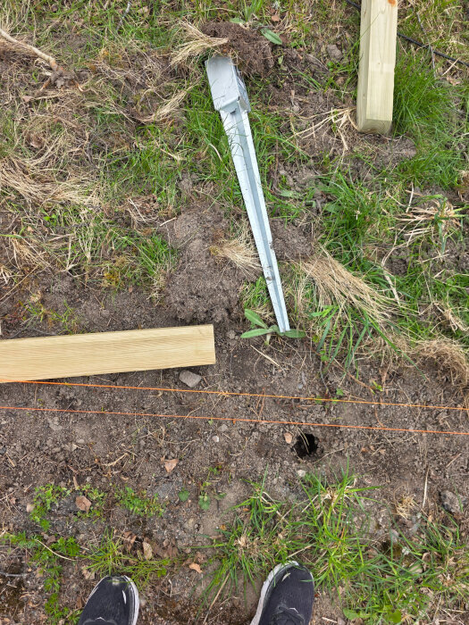 Metallspjut och träbalk vid en gräsmatta, en person står intill.
