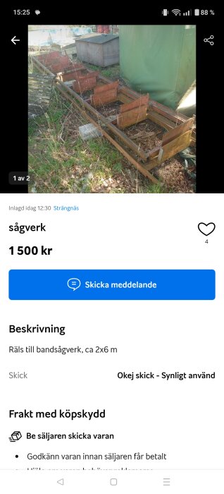 Räls för bandsågverk utomhus, omgiven av gräs och buskar, med en grön presenning och ett brunt skåp i bakgrunden.