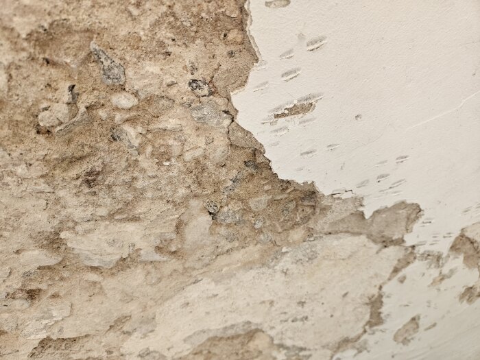 Vägg med sprucken och flagnande puts, synlig grov struktur och skador.