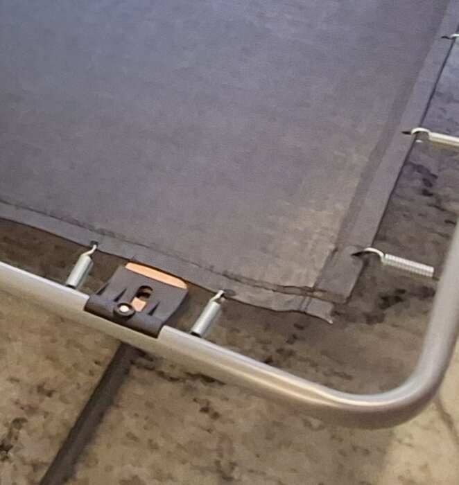 Begagnad bäddsoffas ram och liggduk, med fjädrar som fäster duken mot metallramen. Duken verkar slapp och visar stålstöd på sidan.