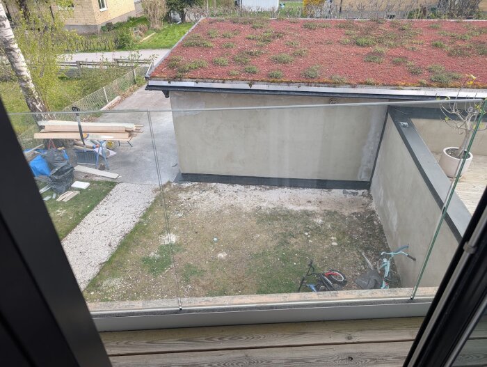 Vy över en innergård med glasräcke, en cykel, diverse byggmaterial och en byggnad med mossbeklätt tak.