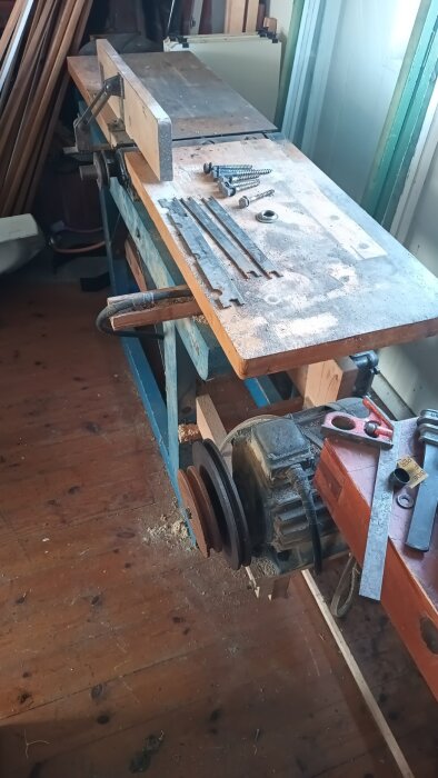 Arbetsbänk i en snickeriverkstad med skruvar, metallbeslag och ett maskinverktyg, del av en gammal snickeriutrustning.