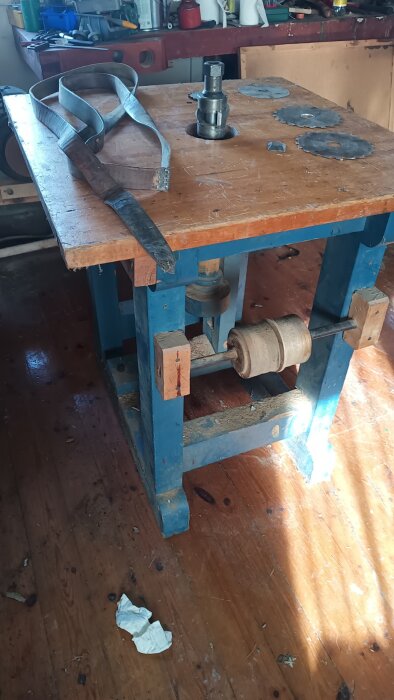 Gammal snickerimaskin med bordsfräs och tillbehör som ligger på verkstadsbänk i en verkstadsmiljö.