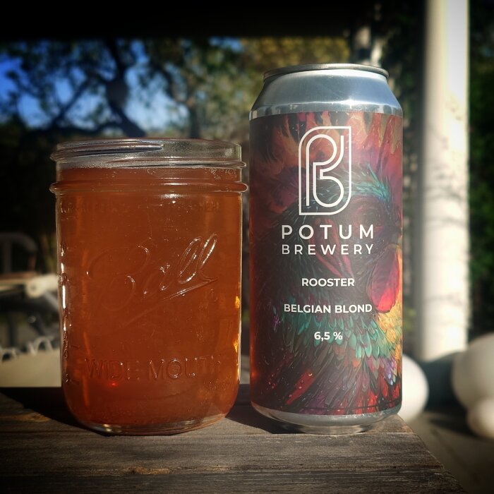 Burk med Potum Brewery Belgian Blond öl och ett glas med öl placerade på ett bord utomhus.