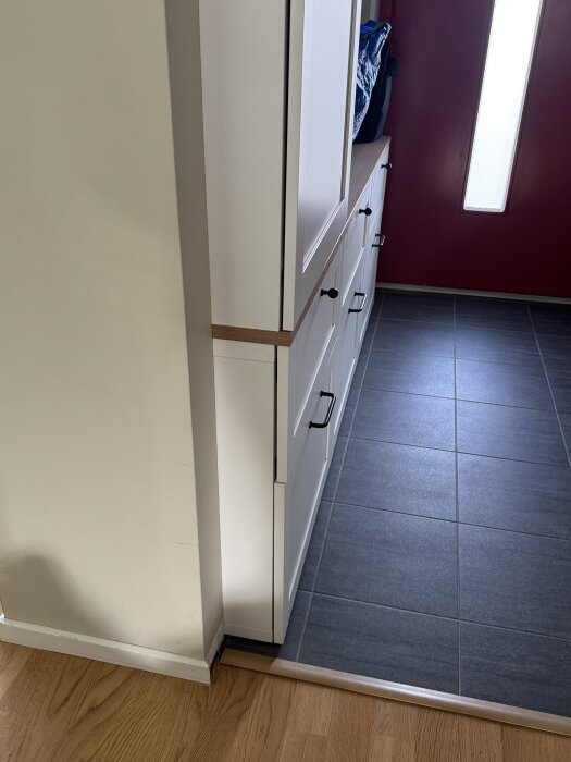 En hallmöbel nära en vägg som behöver förlängas för att möbeln ska se inbyggd ut, med trä- och klinkergolv i ett upplyst rum.