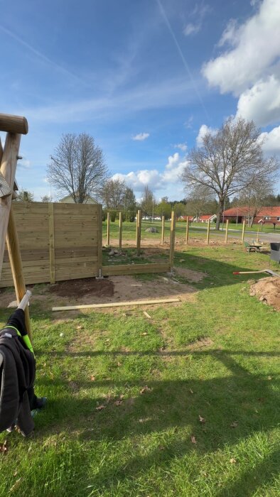 Stolpar och planksektion påbörjade i trädgård under klarblå himmel.
